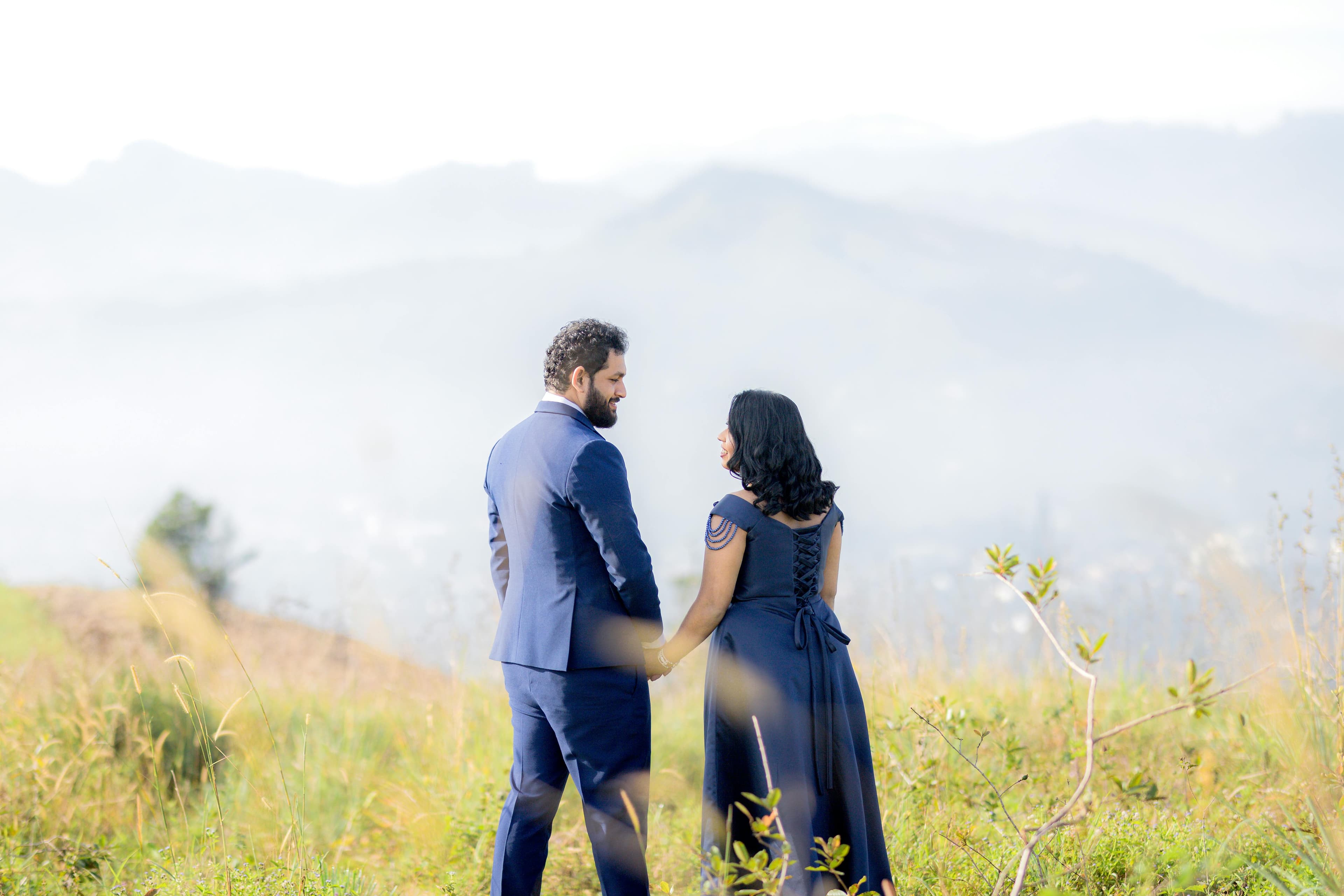 Couple in formal navy attire holding hands in a misty mountain field
